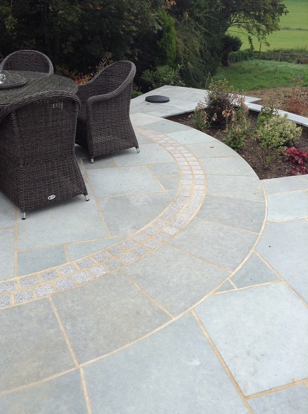 Kota Blue limestone and gravite sett paving circle with gold grout, set into paving next to curved bed. 