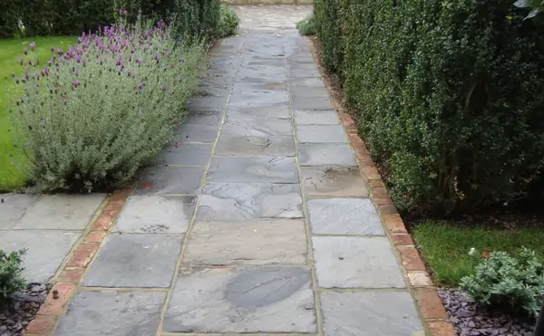 Tumbled black Indian sandstone front path with brick edgeing between lavender and hedge.