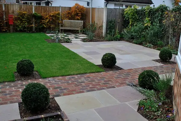 Back garden with 2 staggered patios divided by clay paver path. Box balls and bench.
