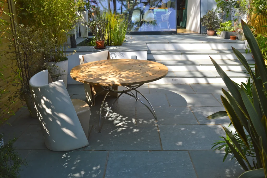 Kota Blue Limestone patio in dappled shade on 2 levels connected with steps with white risers. Round table and chairs in foreground.