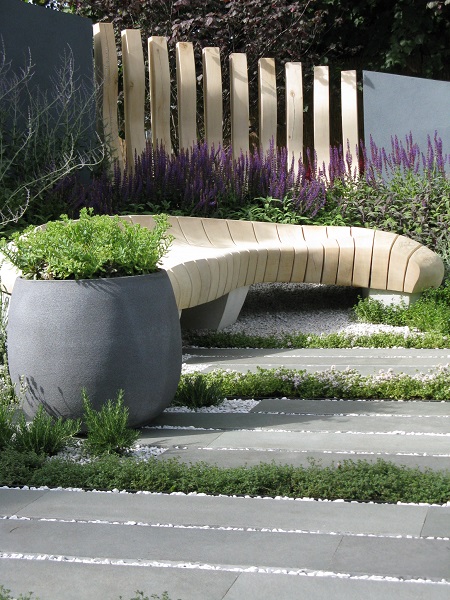 Curved wooden bench with grey pot, kota blue plank paving and gravel in Hampton court show garden 2015
