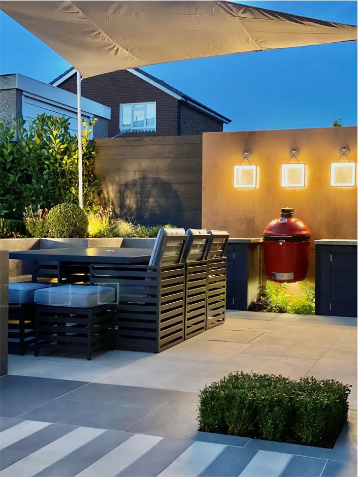 Gas barbecue and cupboards with lighting above, with outdoor dining set on Cream porcelain paving.