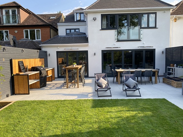 Patio in Florence Grey porcelain paving with outdoor furniture and outdoor kitchen along fence.