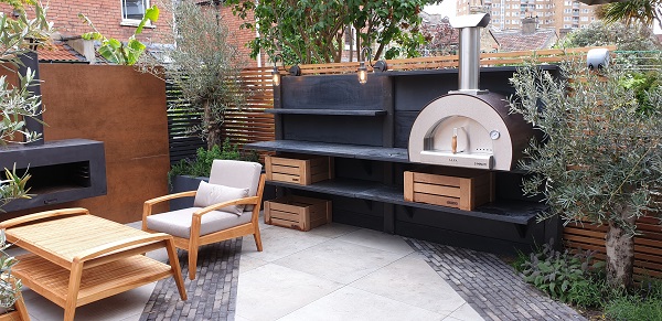 Seating area in corner of garden with Steel Corten Designclad and composite batten fencing, wide black shelves with stell pizza oven.