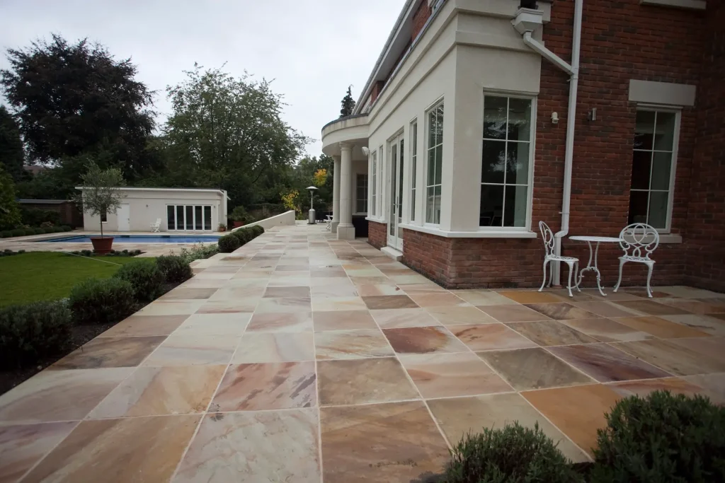 Mint sandstone patio laid stack bond along back of large house with classical portico. Swimming pool to right.