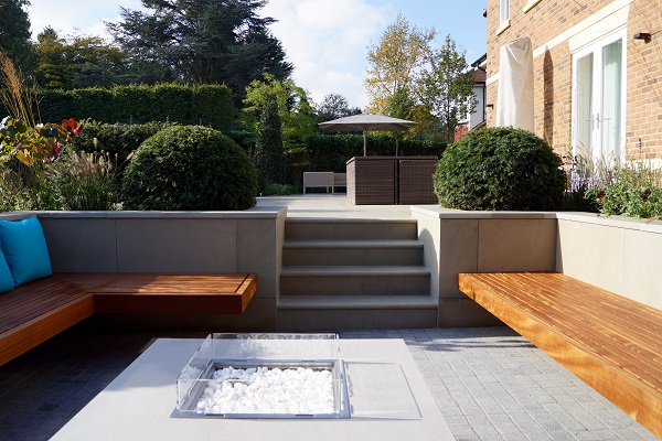 4 steps down from long patio to sunken seating with bench seats and  stone table with fire pit.