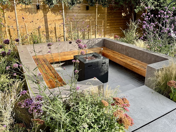 Wooden bench seating in square sunken area with fire pit, faced with Vulcano Ceniza porcelain cladding. 