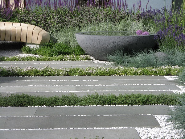 Kota blue limestone plank paving set into white gravel, with planted bowl and curved wooden bench giving a natural stone patio ideas