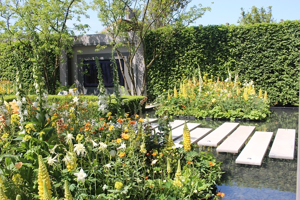 Pond with Jura Grey plank paving forming bridge, planted borders on each side in LG Eco-City Garden,.