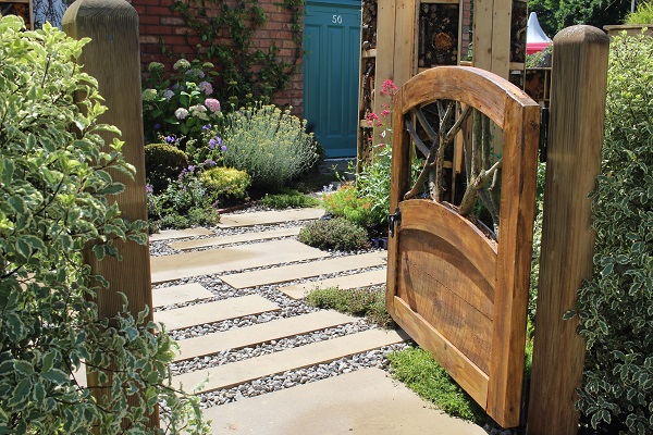 Wooden gate opens onto gravel and buff Yorkstone path with planting in Living in Sync garden, BBC Gardeners' World 2017.