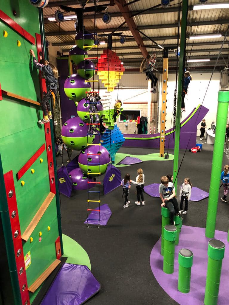Large indoor climbing interior with girls using handholds on wall and others using equipment.