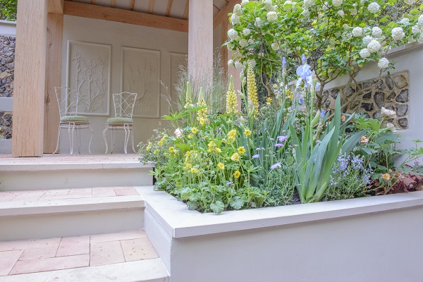 Natural stone patio ideas of raised bed with Harvest sawn sandstone coping on level with tread of steps up to chairs.