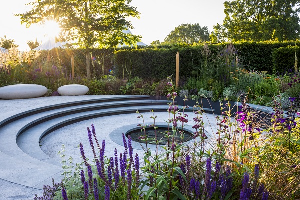 Curved steps descend to round pond edged with Jura Green coping in Tom Simpson's Cancer Research garden, RHS Hampton Court 2019. 