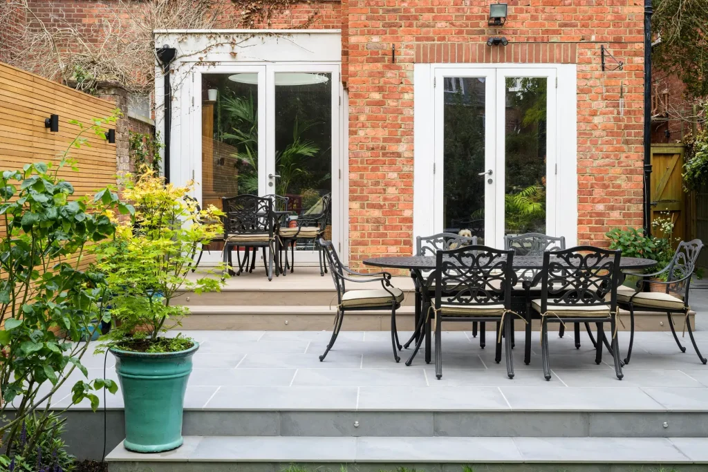 Metal dining set on patio of Florence Storm dark grey porcelain outside tiles with 2 steps up to french doors. Green plant pot on left.