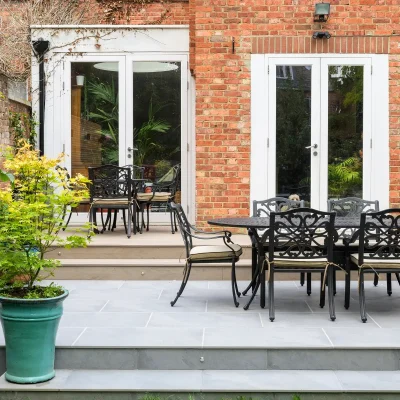 Metal dining set on patio of Florence Storm dark grey porcelain outside tiles with 2 steps up to french doors. Green plant pot on left.