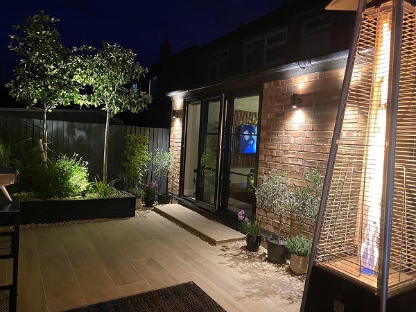 Illuminated patio of Rovere wood-effect porcelain planks at back of house with bifold doors .