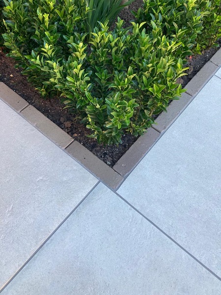 Corner of flower bed with Florence Grey vitrified paving on 2 sides and single width stone paver patio edging.