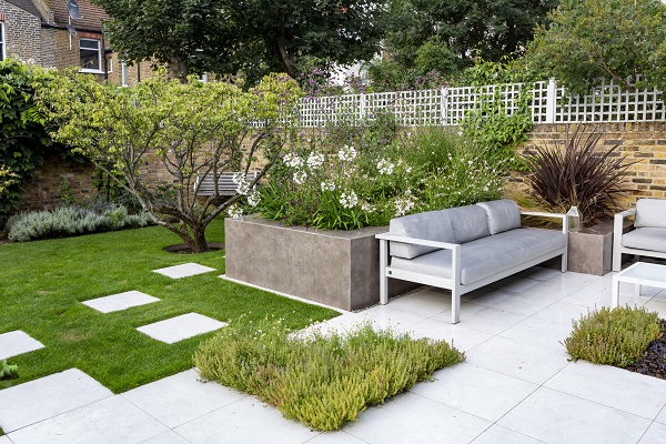 Patio edged by lushly planted raised beds faced by Vulcano Ceniza DesignClad. 