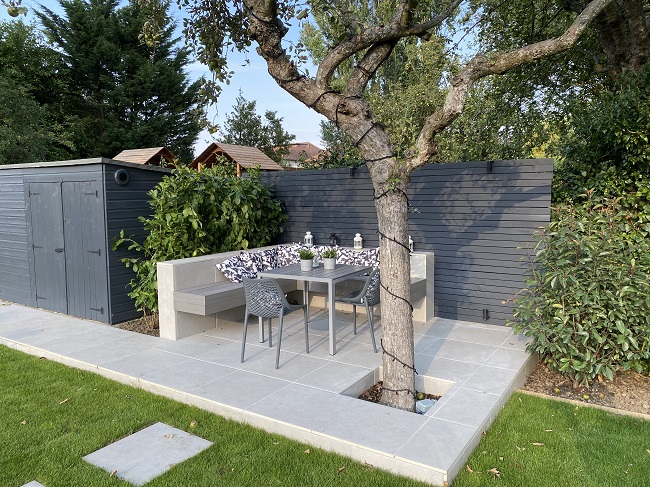 Florence Grey porcelain patio with tree pit and outdoor dining set. Dark fence behind. 