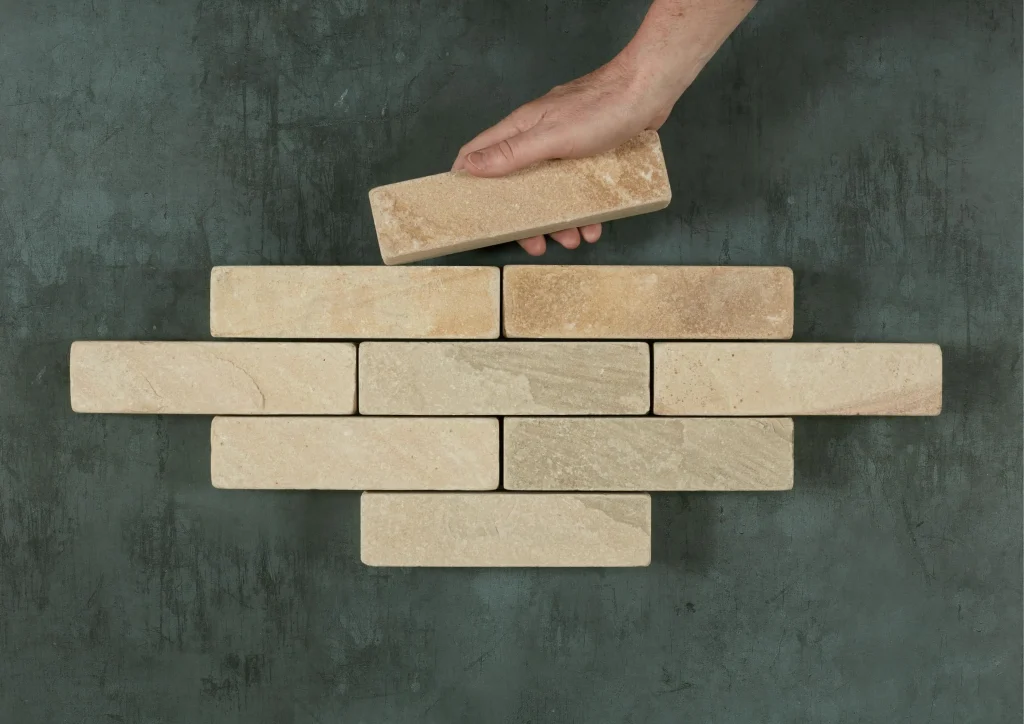 A hand places a 9th Mint sandstone patio brick to complete a lozenge shape with 8 other bricks.