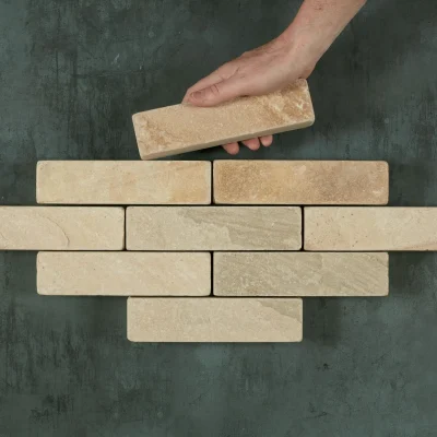A hand places a 9th Mint sandstone patio brick to complete a lozenge shape with 8 other bricks.