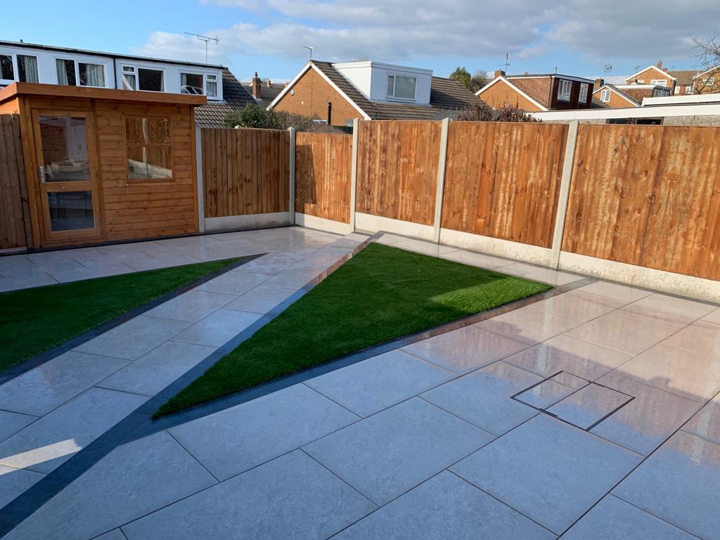 Path crosses lawn from corner to corner from patio to narrow paved area in fenced garden. 