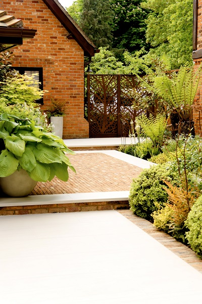 Clay paver patio edged with Faro porcelain paving, sits between 2 paved areas with planting on 2 sides.