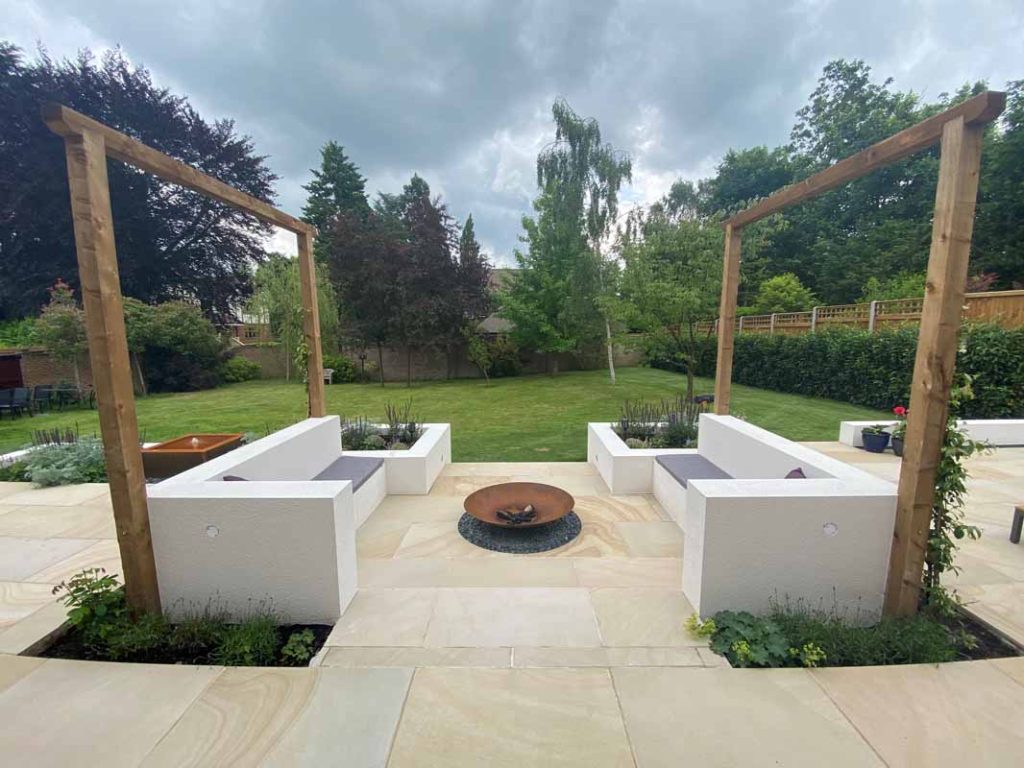 Light Buff sawn sandstone patio with white modern sofas facing each other across fire pit. Lawn beyond.