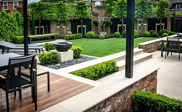 View across garden from raised patio with decking to lawn and pleached trees against boundary fence.