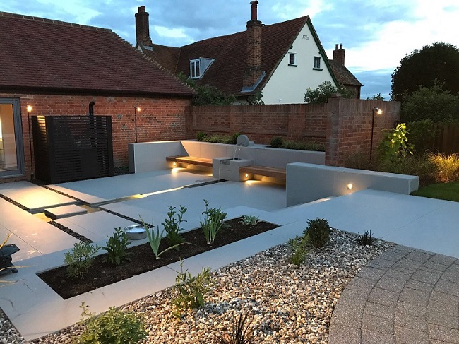 Urban Grey porcelain slabs laid in rectlinear design divided by rills at back of country cottage. 