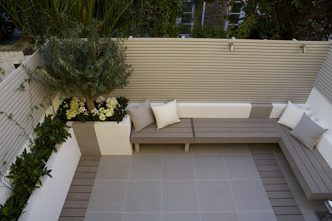 Small urban back garden fully paved with Urban Grey porcelain paving and composite decking. With raised bed edges and inbuilt benches.