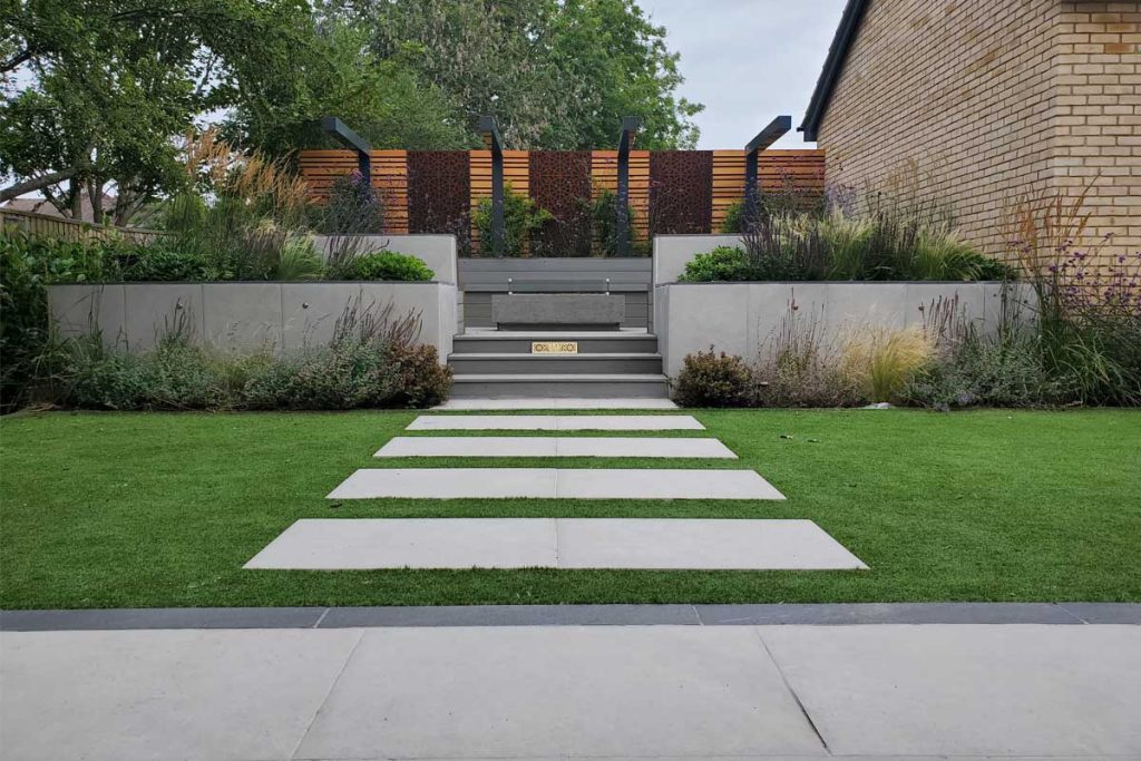 Florence Grey paving spaced across lawn to steps between flanking beds to raised seating area 