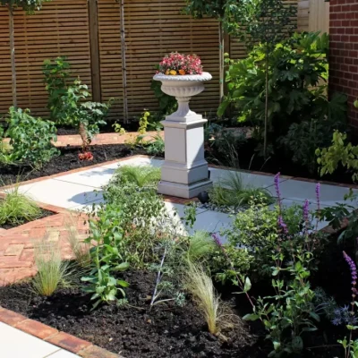 Flower filled urn on pedestal in symmetrical paved area of Venetian Beige porcelain paving edged with clay pavers.