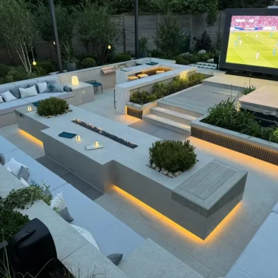 Large sunken seating area with sofas on 3 sides and long firepit table, in party garden with large TV screen