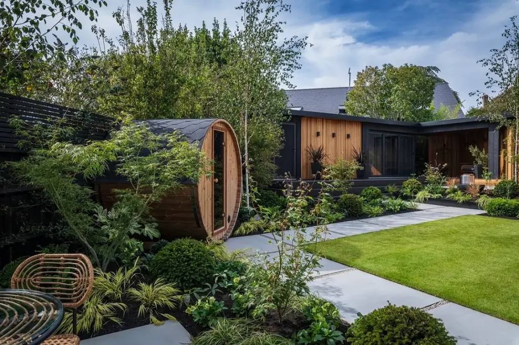 Path of Yard porcelain paving edges square lawn and passes barrel garden room and planted beds.