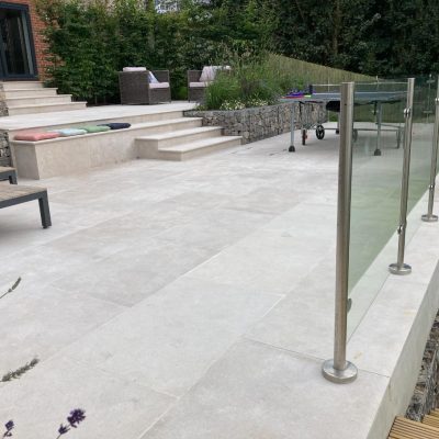 Terraced Egyptian beige limestone patio descend from house via matching steps, with raised beds of stone-filled gabions.