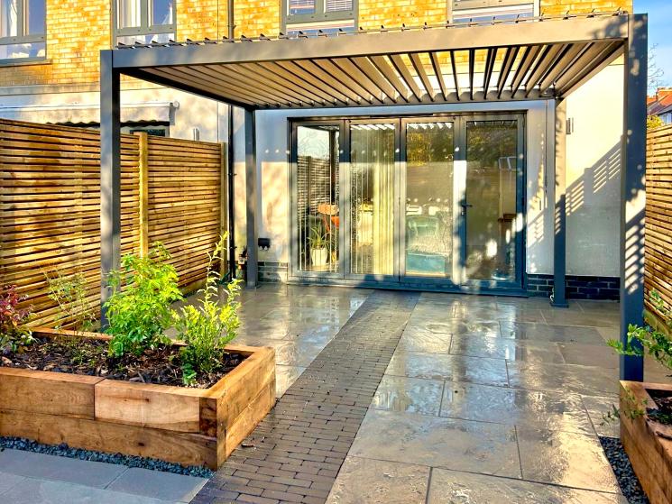 Patio covered by open louvred pergola, looking at back of house
