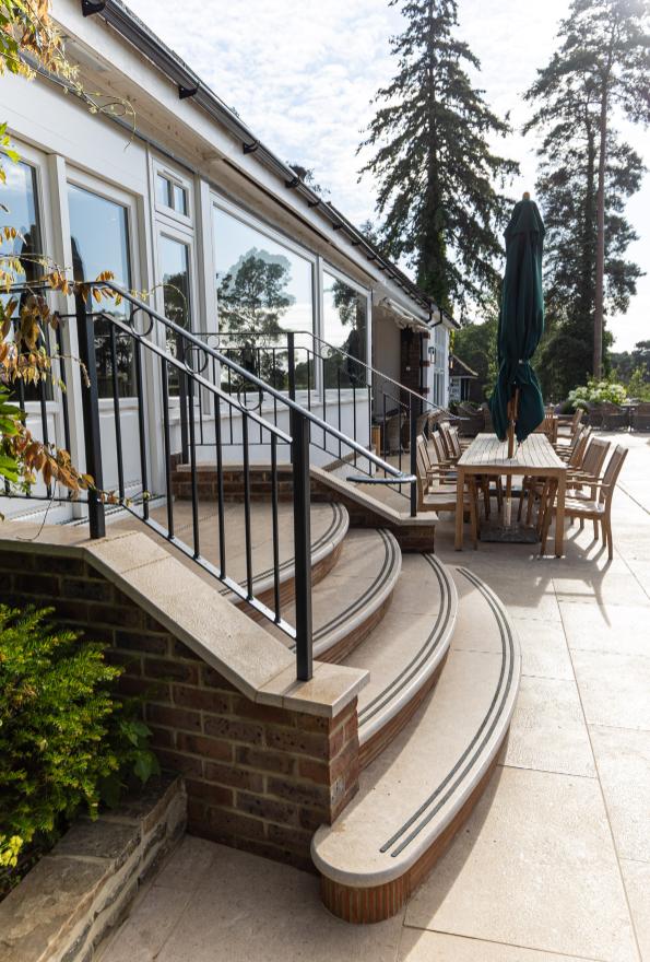 4 Curved steps rise between iron hand rails, from golf club terrace of Egyptian Beige limestone to double doors.