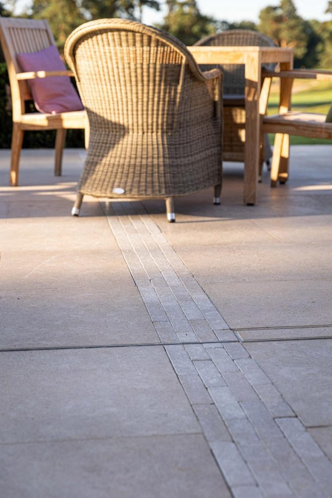 Egyptian Beige limestone paving slabs with strip of matching stone pavers inserted. Chair in background.