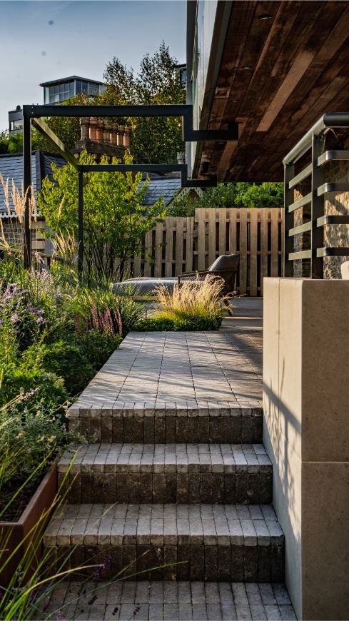 Clay paver steps rise past Florence Grey porcelain clad wall to patio.