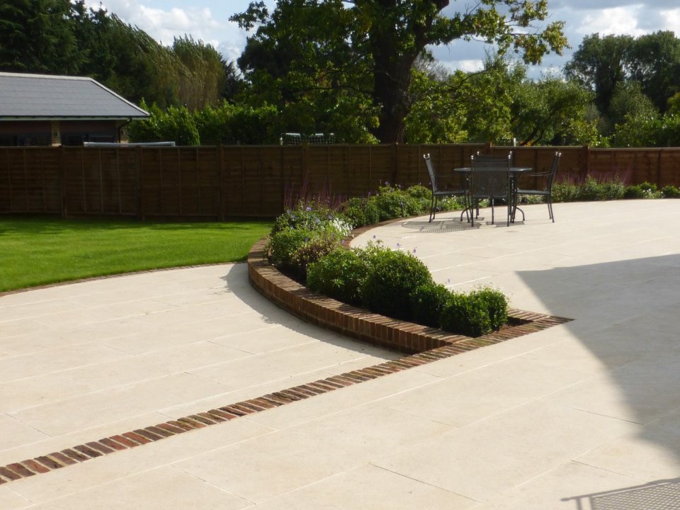 Large patio of Golden Stone Porcelain Paving with clay paver edging and step.
