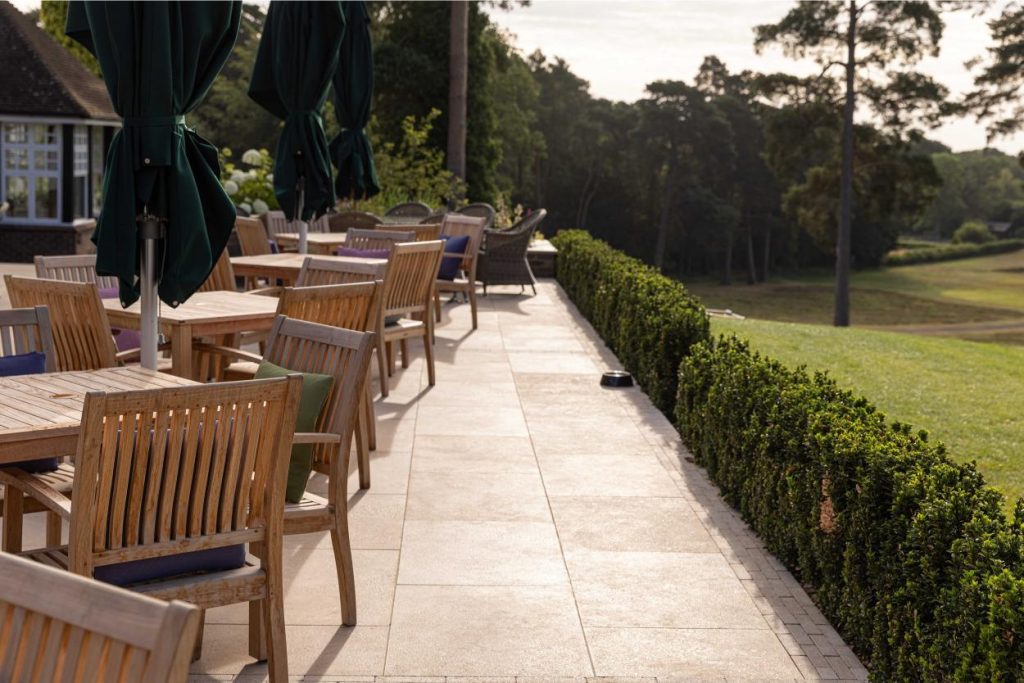 Edge of long terrace of Egyptian Beige limestone, edged with low hedge. Seating to left.