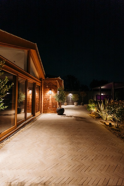 Illuminated night view of fire pit with in-built seating and Egyptian Beige stone paving. House behind.