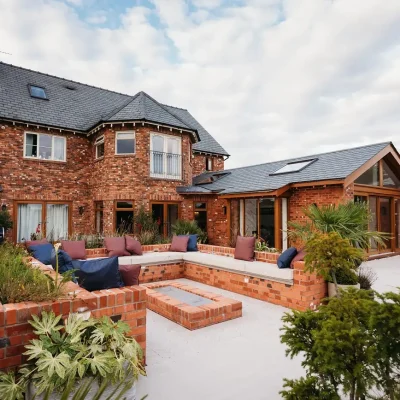 Patio wraps around rear of house with low brick walls, firepit and light-coloured paving
