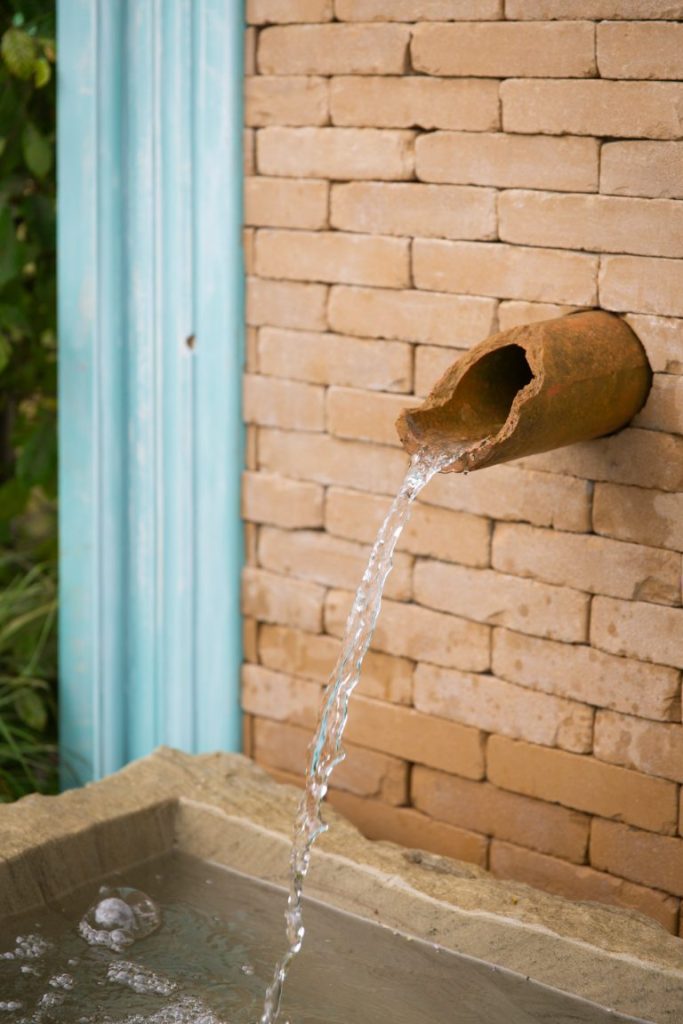 Broken terracotta waterspout set into wall of Golden Buff clay pavers.