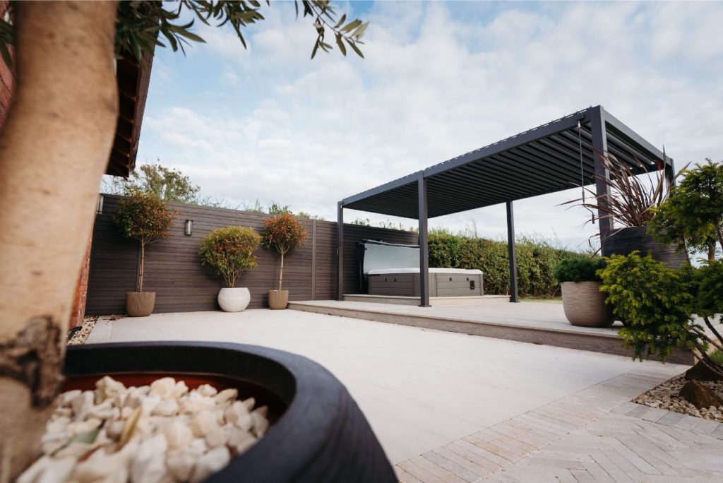 Faro porcelain paving between raised deck area with hot tub and pergola and edge of Egyptian Beige stone brick pavers.