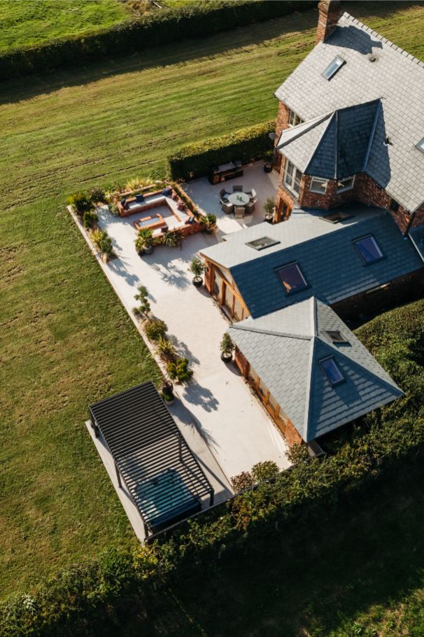 Overhead viiew of large patio of Faro porcelain paving and Egyptian limesotne pavers across width of property in big lawn.