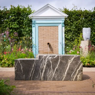 Large solid rock seat in front of water feature of door frame and Golden Buff clay pavers in RHS Wentworth show garden.