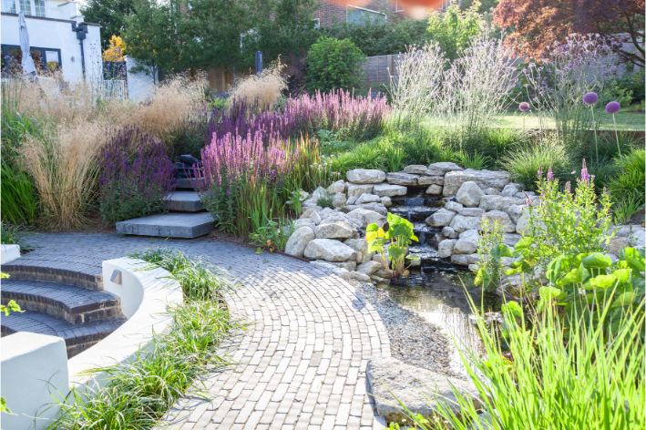 Curved path of Moderna clay pavers runs between sunken seating and cascading water feature