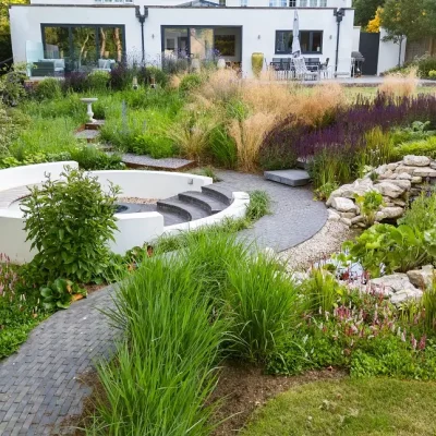 View up garden to white house. Curved path winds between sunken seating and cascading water feature